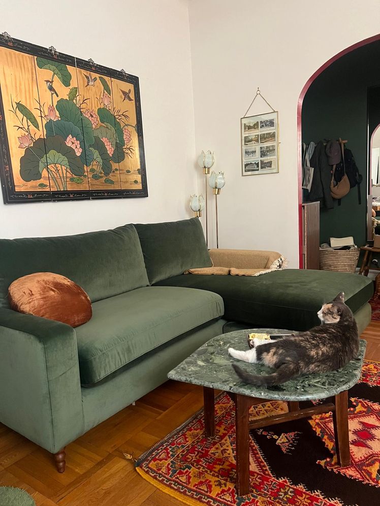 Living room with a green velvet sectional couch with a chaise and a mrable table in front of it with a cat resting on it.